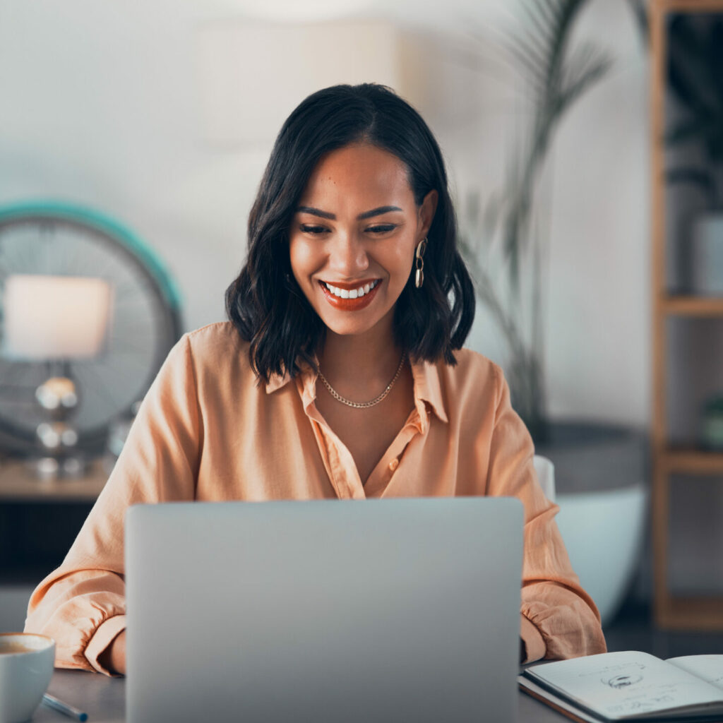 BIPOC woman looking at her computer wearing an orange shirt smiling